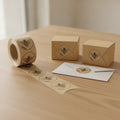 Custom logo stickers on a kraft brown roll, unrolled beside kraft boxes sealed with 2 inch round logo labels
