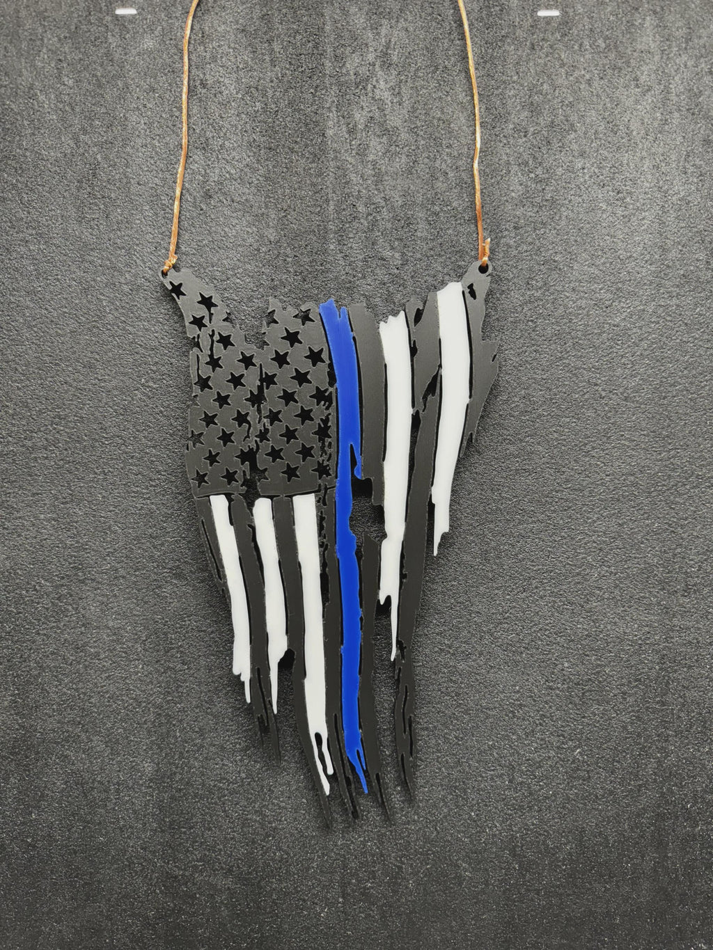Tattered American flag wall decor in black with white stripes and one blue stripe, hanging from a cord on a gray background