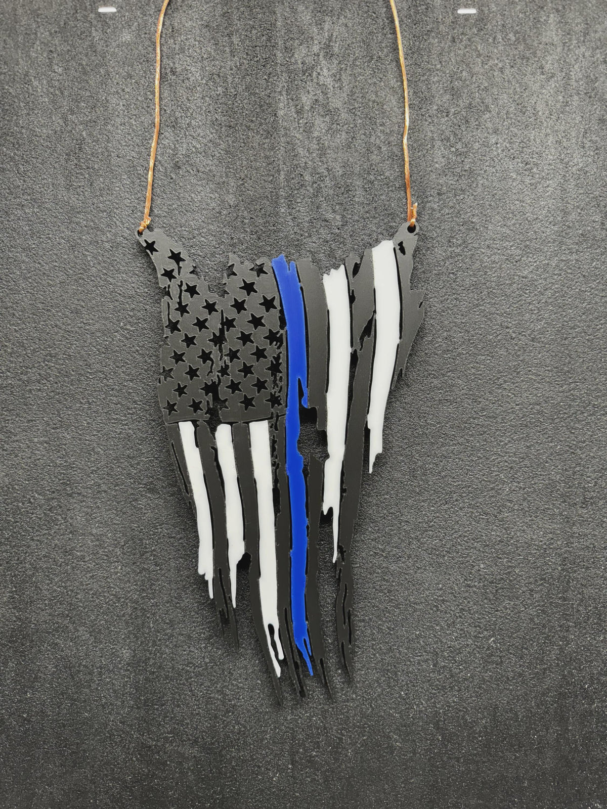Tattered American flag wall decor in black with white stripes and one blue stripe, hanging from a cord on a gray background