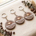 Three custom 3D logo keychains with Maple & Main Coffee Co. cup logo, brown and cream, on cream fabric with coffee beans