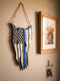 Tattered American flag wall decor with a blue stripe, hung by a leather cord beside a framed family picture and key hooks
