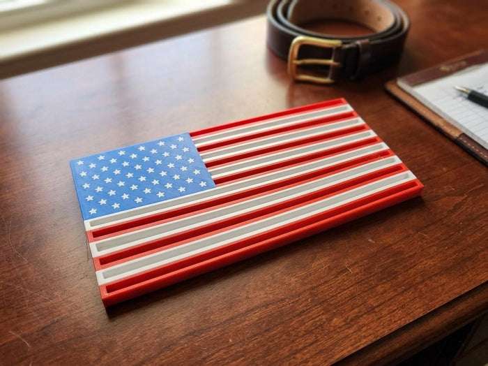 Thin Line Flag challenge coin display in red, white and blue with star field, on a wooden desk beside a belt and notepad