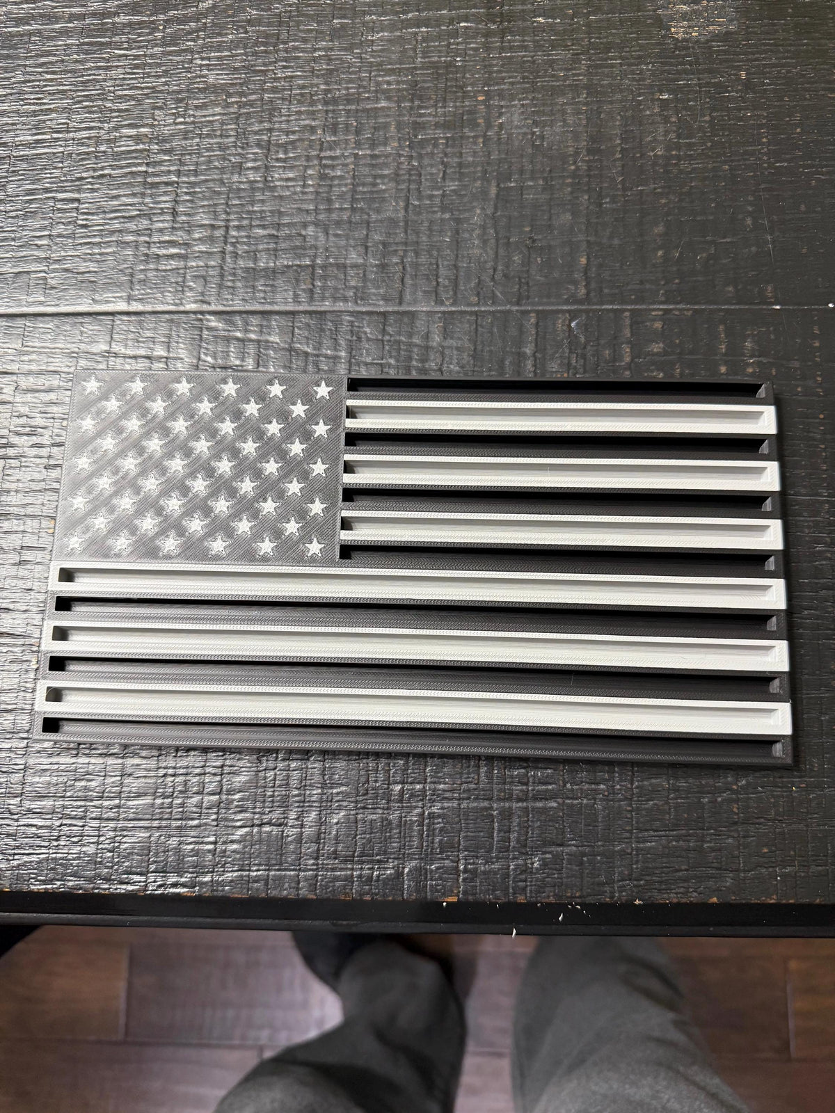 Thin Line Flag Challenge Coin Display, black and gray American flag with slotted stripes, on a dark rustic wooden table