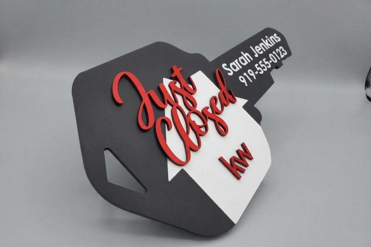 Black key-shaped Realtor sold sign with red "Just Closed" script, white house, kw logo and sample agent name and phone